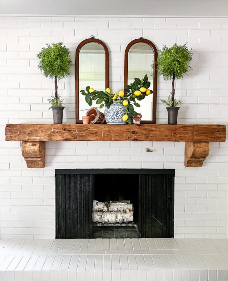 A simple summer mantel decorated with topiaries, lemon stems, a ginger jar and terracota pots.